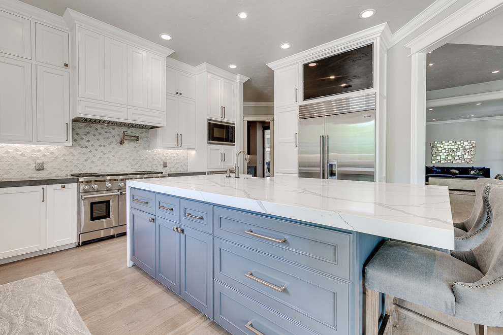 Inspiration for a large transitional l-shaped light wood floor enclosed kitchen remodel in Nashville with a farmhouse sink, recessed-panel cabinets, white cabinets, quartz countertops, gray backsplash, metal backsplash, stainless steel appliances and an island