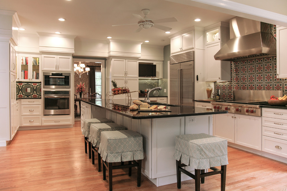 Exempel på ett stort, avskilt klassiskt svart svart u-kök, med skåp i shakerstil, vita skåp, en köksö, granitbänkskiva, en undermonterad diskho, rött stänkskydd, stänkskydd i keramik, rostfria vitvaror, ljust trägolv och brunt golv