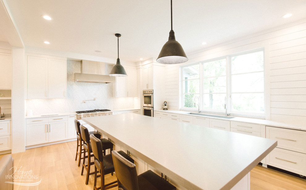 Cette image montre une cuisine avec des portes de placard blanches, une crédence blanche, un électroménager en acier inoxydable et îlot.