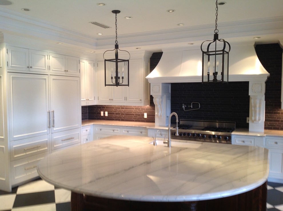 Inredning av ett klassiskt stort kök, med en undermonterad diskho, luckor med upphöjd panel, vita skåp, granitbänkskiva, svart stänkskydd, stänkskydd i keramik, rostfria vitvaror, marmorgolv och en köksö
