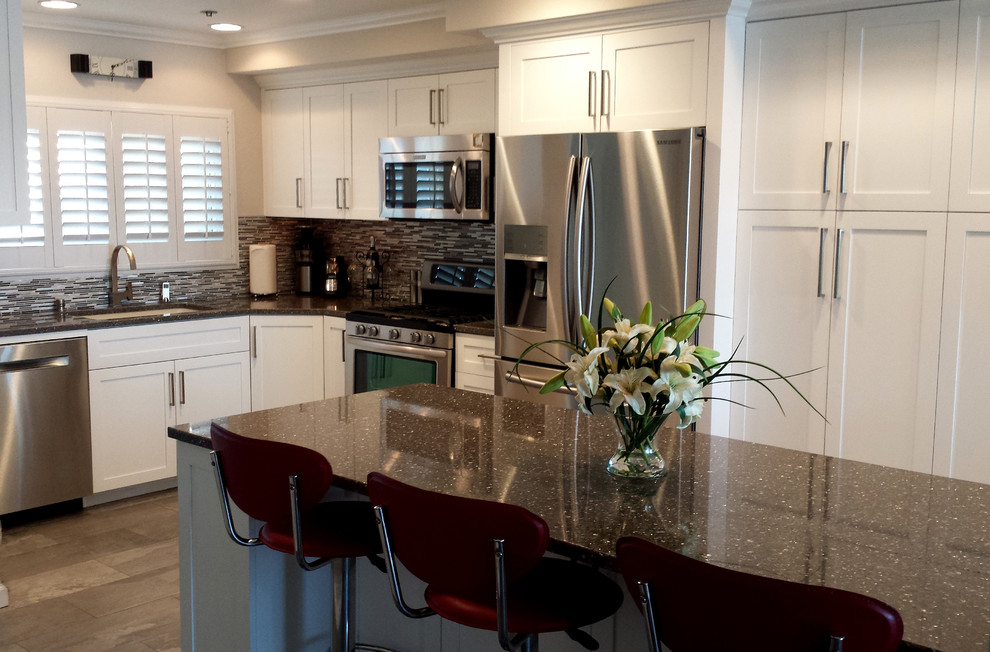 Example of a mid-sized trendy l-shaped porcelain tile eat-in kitchen design in Los Angeles with an undermount sink, shaker cabinets, white cabinets, quartz countertops, metallic backsplash, mosaic tile backsplash, stainless steel appliances and an island