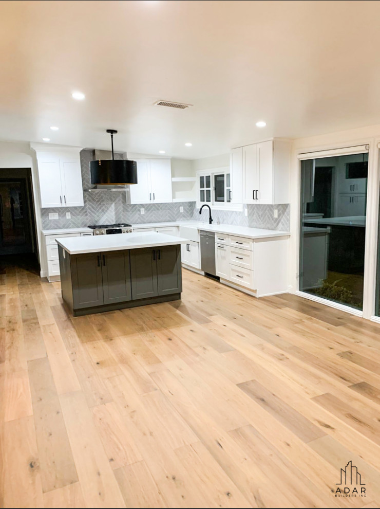 Foto på ett stort funkis vit kök, med luckor med infälld panel, vita skåp, marmorbänkskiva, grått stänkskydd, stänkskydd i tunnelbanekakel, rostfria vitvaror, ljust trägolv, en köksö och beiget golv