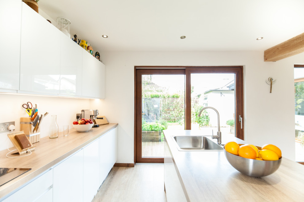 Immagine di una cucina moderna di medie dimensioni con ante lisce, ante bianche, top in legno e pavimento in laminato