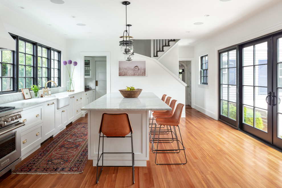 Landhausstil Küche mit Kücheninsel, Landhausspüle, Schrankfronten im Shaker-Stil, weißen Schränken, Küchengeräten aus Edelstahl, braunem Holzboden und grauer Arbeitsplatte in Boston