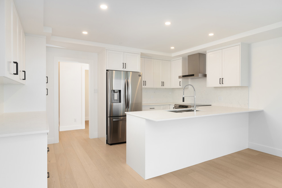 Idéer för att renovera ett avskilt, mellanstort funkis vit vitt u-kök, med en undermonterad diskho, skåp i shakerstil, vita skåp, bänkskiva i kvarts, vitt stänkskydd, rostfria vitvaror, ljust trägolv, en köksö och grått golv