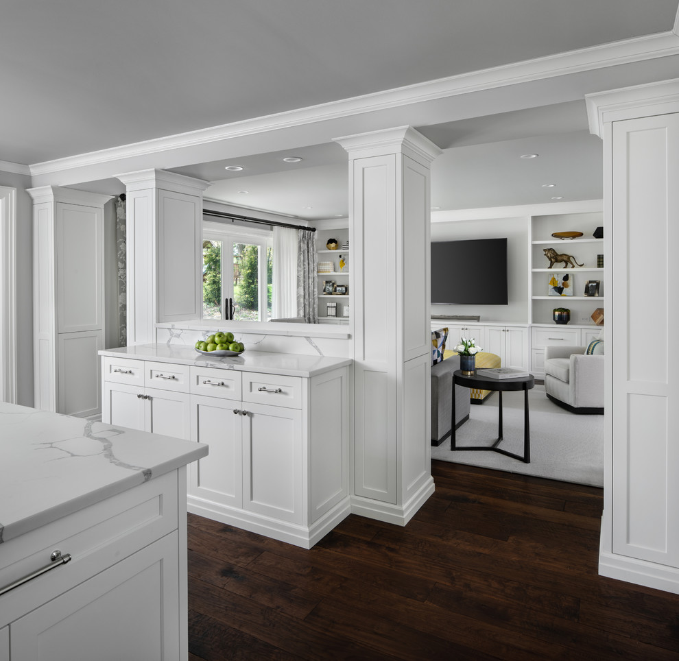Klassisk inredning av ett mycket stort vit linjärt vitt kök och matrum, med en undermonterad diskho, luckor med upphöjd panel, vita skåp, marmorbänkskiva, vitt stänkskydd, stänkskydd i marmor, integrerade vitvaror, mörkt trägolv, en köksö och brunt golv
