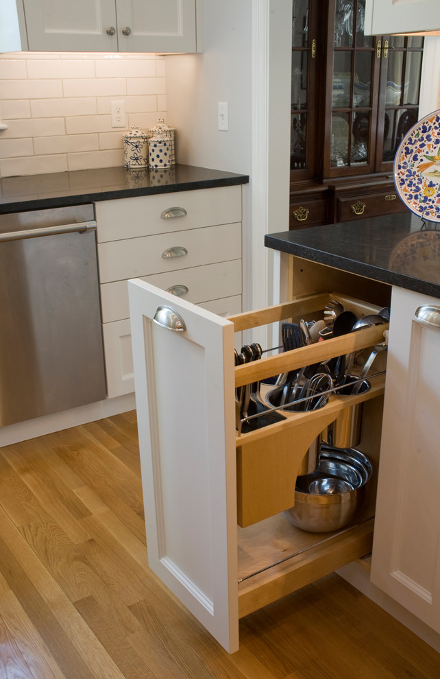 Klassische Küche mit Schrankfronten mit vertiefter Füllung, weißen Schränken, Granit-Arbeitsplatte, Küchenrückwand in Weiß, Rückwand aus Keramikfliesen, Küchengeräten aus Edelstahl, braunem Holzboden und schwarzer Arbeitsplatte in Boston