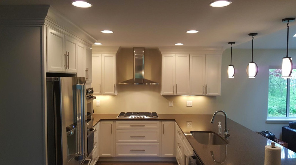 This is an example of a medium sized classic u-shaped open plan kitchen in Other with a submerged sink, recessed-panel cabinets, white cabinets, composite countertops, stainless steel appliances, medium hardwood flooring, a breakfast bar and brown floors.
