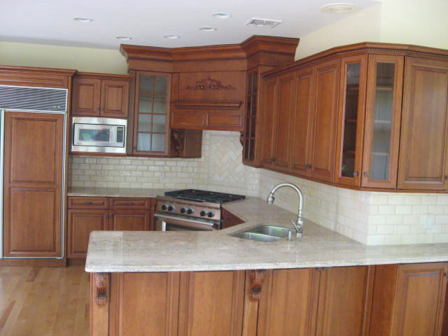 This is an example of a medium sized classic u-shaped open plan kitchen in New York with a double-bowl sink, raised-panel cabinets, medium wood cabinets, granite worktops, white splashback, metro tiled splashback, integrated appliances, light hardwood flooring, a breakfast bar, beige floors and grey worktops.