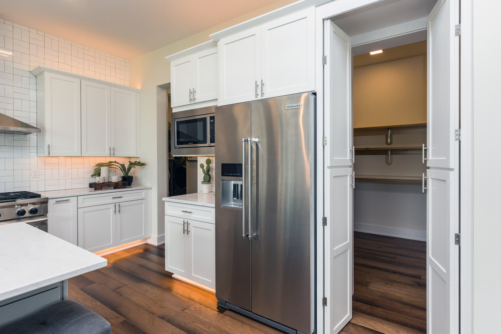 Inspiration for a large transitional l-shaped medium tone wood floor and brown floor eat-in kitchen remodel in Other with an undermount sink, shaker cabinets, white cabinets, quartz countertops, white backsplash, stainless steel appliances, an island and subway tile backsplash