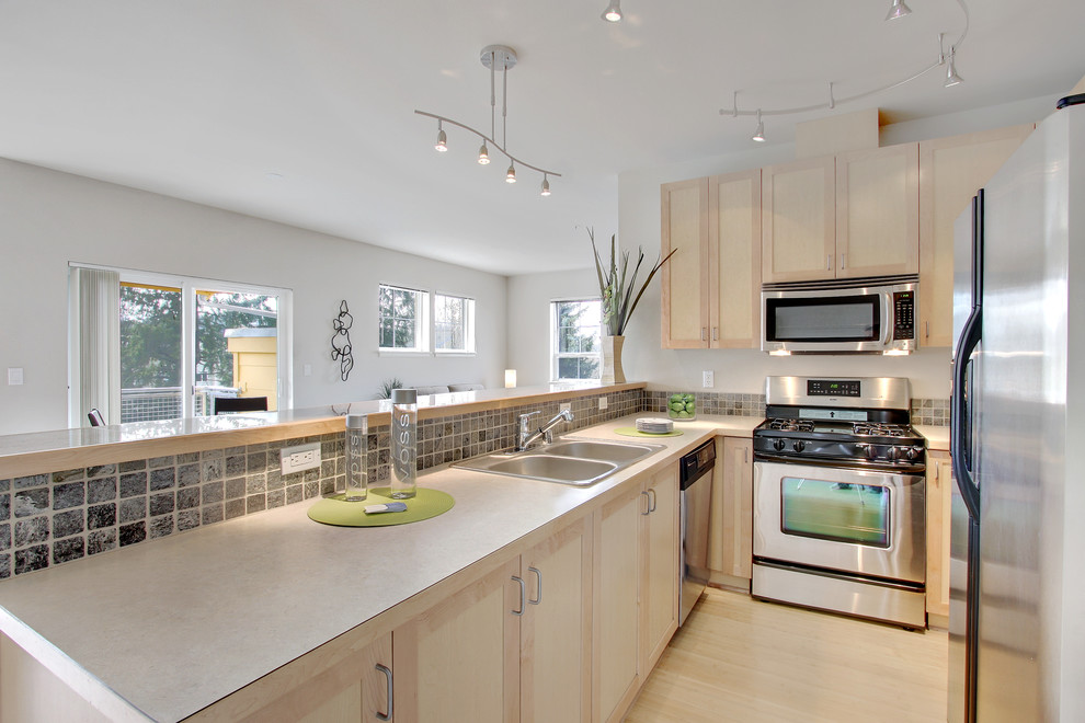 Medium sized contemporary galley open plan kitchen in Seattle with a built-in sink, shaker cabinets, medium wood cabinets, laminate countertops, grey splashback, stone tiled splashback, stainless steel appliances, light hardwood flooring, a breakfast bar and beige floors.