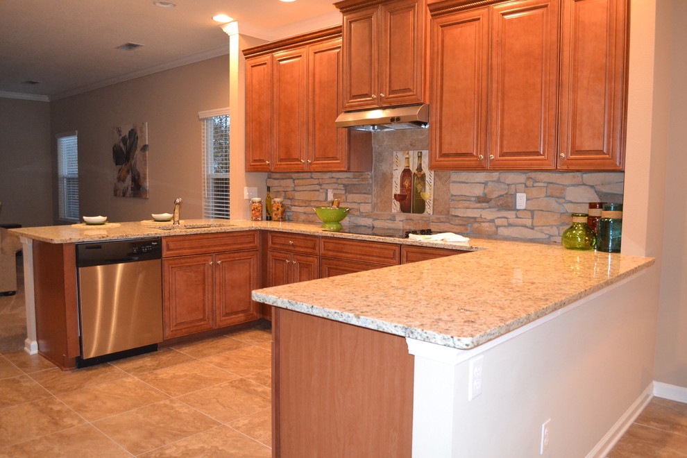 Inredning av ett klassiskt mellanstort u-kök, med en undermonterad diskho, luckor med upphöjd panel, skåp i mellenmörkt trä, granitbänkskiva, beige stänkskydd, stänkskydd i stenkakel, rostfria vitvaror, klinkergolv i porslin och en halv köksö