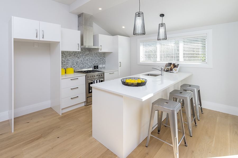 Photo of a small contemporary single-wall kitchen/diner in Auckland with a single-bowl sink, flat-panel cabinets, white cabinets, grey splashback, mosaic tiled splashback, stainless steel appliances and light hardwood flooring.