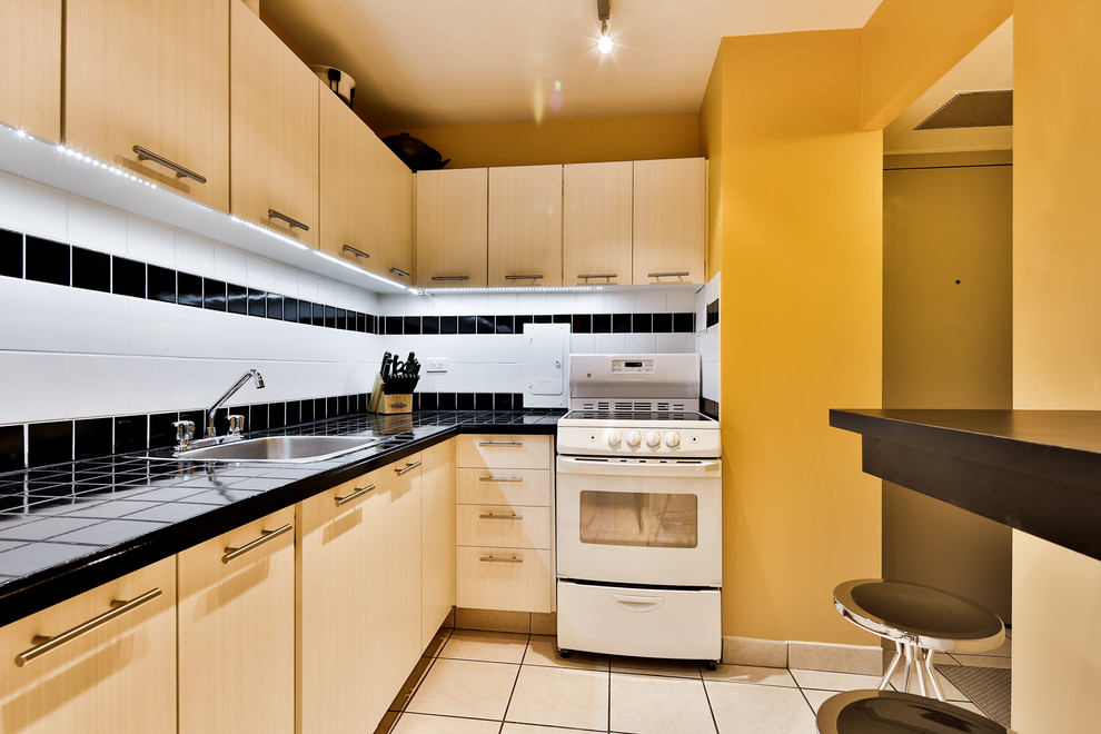 モントリオールにある低価格の小さなコンテンポラリースタイルのおしゃれなキッチン (シングルシンク、フラットパネル扉のキャビネット、淡色木目調キャビネット、タイルカウンター、白いキッチンパネル、セラミックタイルのキッチンパネル、白い調理設備、セラミックタイルの床、アイランドなし) の写真