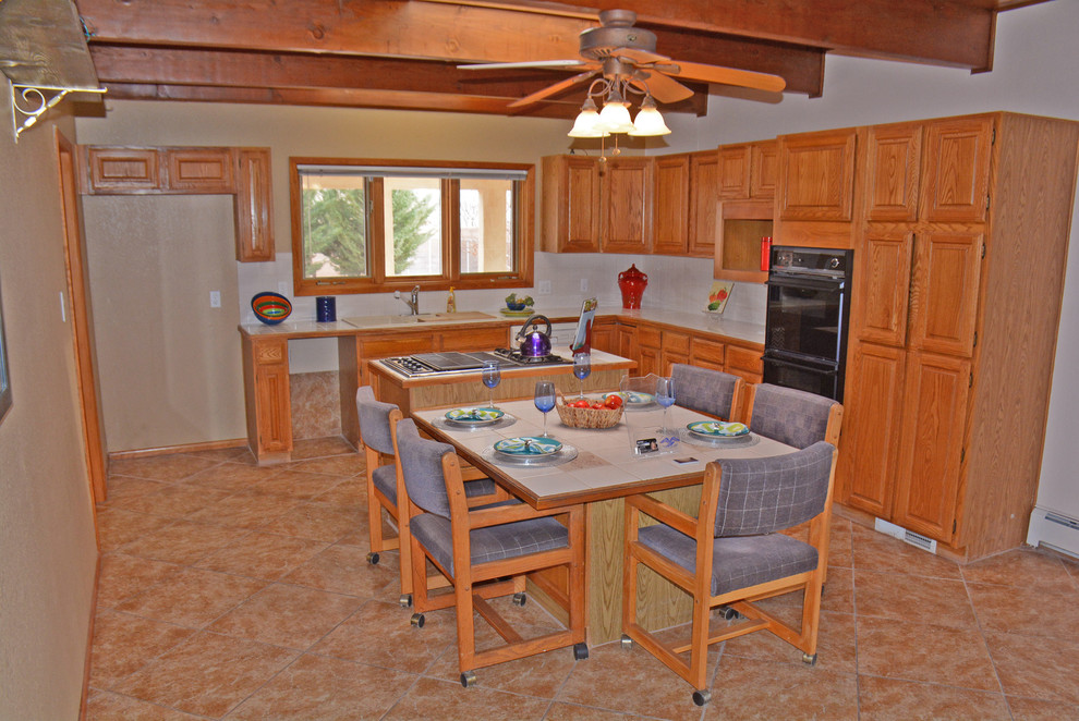Example of a mid-sized southwest l-shaped ceramic tile open concept kitchen design in Albuquerque with a double-bowl sink, raised-panel cabinets, light wood cabinets, tile countertops, white backsplash, subway tile backsplash, black appliances and an island
