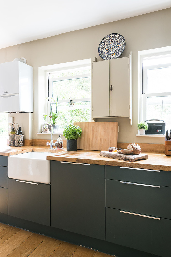 Landhaus Küche mit Landhausspüle, flächenbündigen Schrankfronten, schwarzen Schränken, Arbeitsplatte aus Holz, hellem Holzboden und Mauersteinen in London