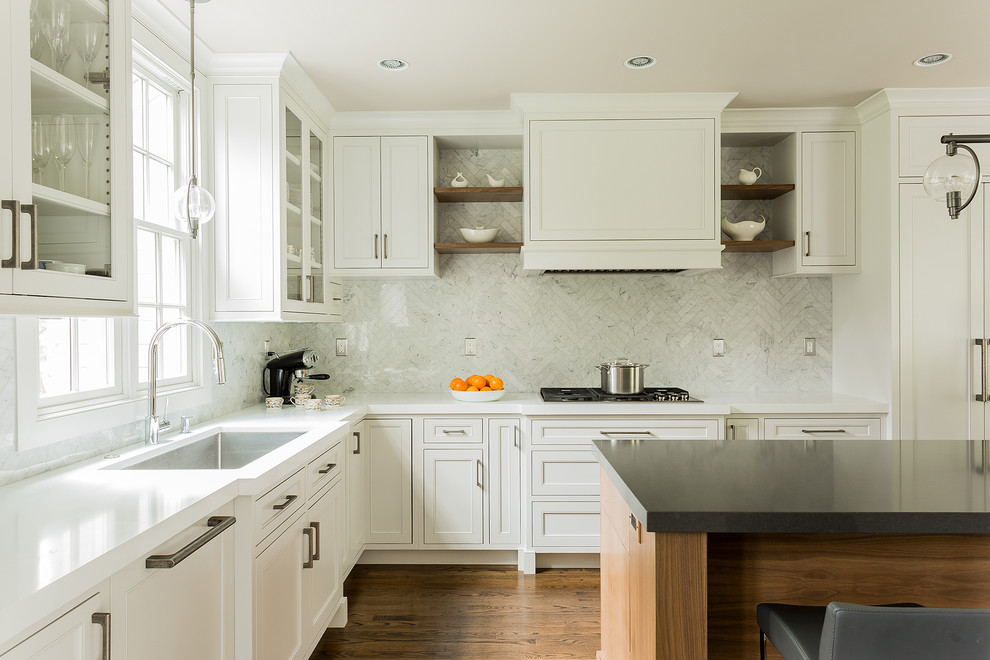 Klassisk inredning av ett kök, med en undermonterad diskho, skåp i shakerstil, vita skåp, bänkskiva i kvarts, vitt stänkskydd, stänkskydd i stenkakel, rostfria vitvaror, mellanmörkt trägolv och en köksö