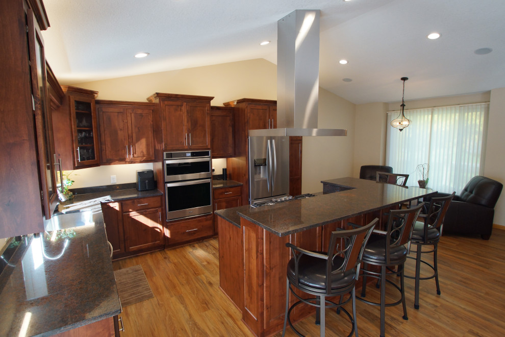 This is an example of a medium sized traditional l-shaped kitchen/diner in Minneapolis with a submerged sink, flat-panel cabinets, dark wood cabinets, granite worktops, stainless steel appliances, vinyl flooring, an island, brown floors and black worktops.