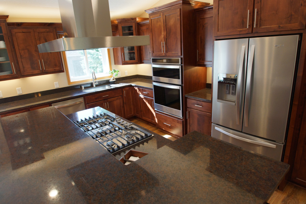 Design ideas for a medium sized classic l-shaped kitchen/diner in Minneapolis with a submerged sink, flat-panel cabinets, dark wood cabinets, granite worktops, stainless steel appliances, vinyl flooring, an island, brown floors and black worktops.