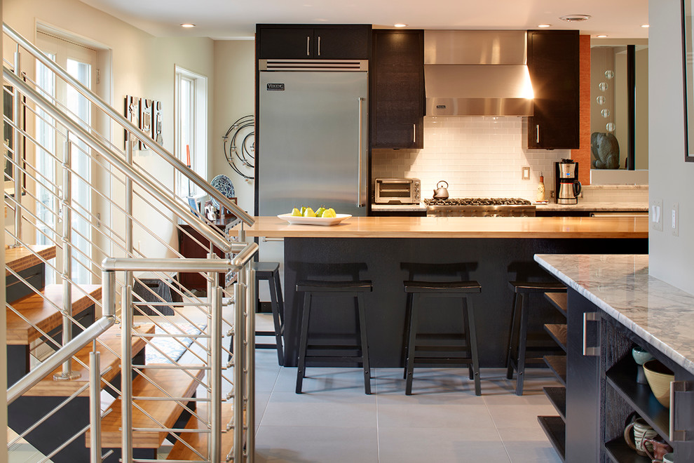 Foto på ett mellanstort funkis grå kök, med släta luckor, svarta skåp, marmorbänkskiva, vitt stänkskydd, rostfria vitvaror, en köksö, stänkskydd i glaskakel, en undermonterad diskho, klinkergolv i porslin och grått golv