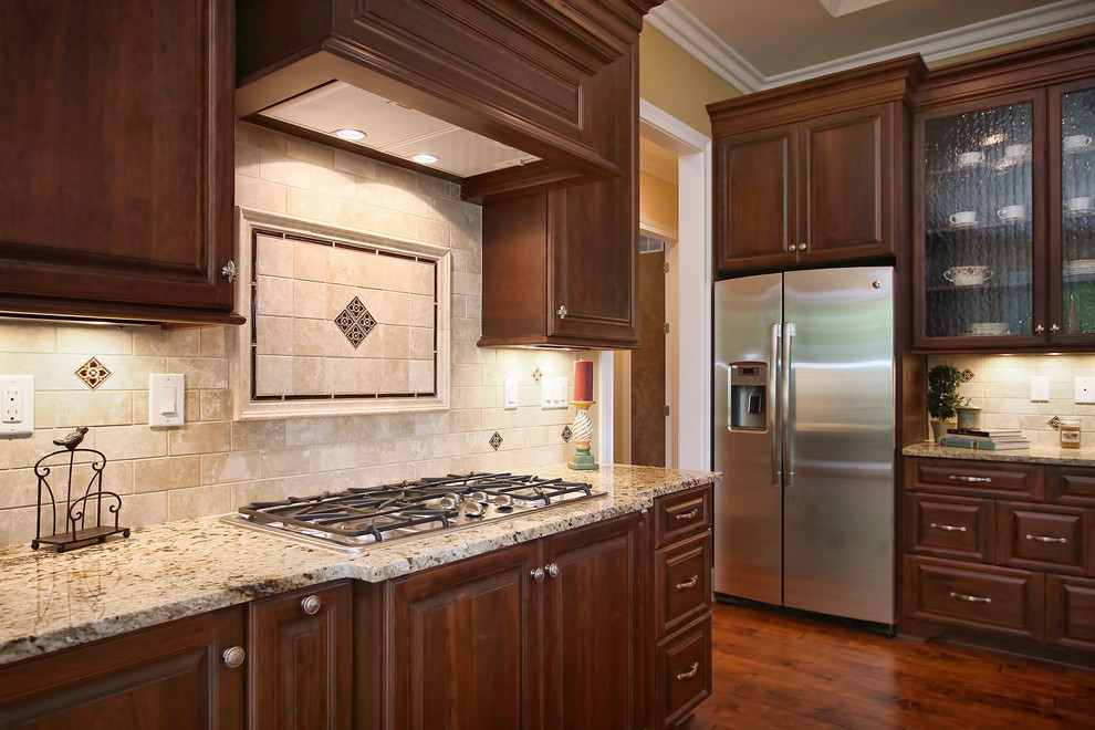 Mid-sized elegant l-shaped medium tone wood floor open concept kitchen photo in Louisville with a drop-in sink, raised-panel cabinets, medium tone wood cabinets, granite countertops, beige backsplash, stone tile backsplash, stainless steel appliances and an island