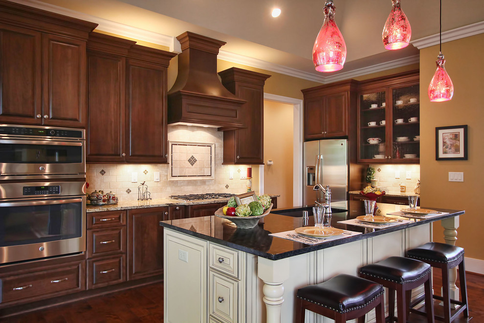 Inspiration for a mid-sized timeless l-shaped medium tone wood floor open concept kitchen remodel in Louisville with a drop-in sink, raised-panel cabinets, medium tone wood cabinets, granite countertops, beige backsplash, stone tile backsplash, stainless steel appliances and an island