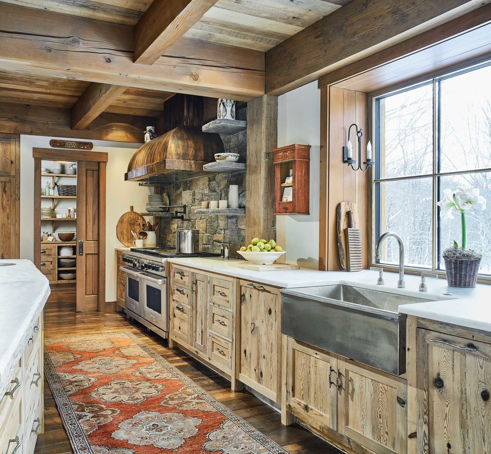 Photo of a rustic galley kitchen in Burlington with a belfast sink, shaker cabinets, light wood cabinets, grey splashback, stone tiled splashback, stainless steel appliances, medium hardwood flooring, an island, brown floors and white worktops.