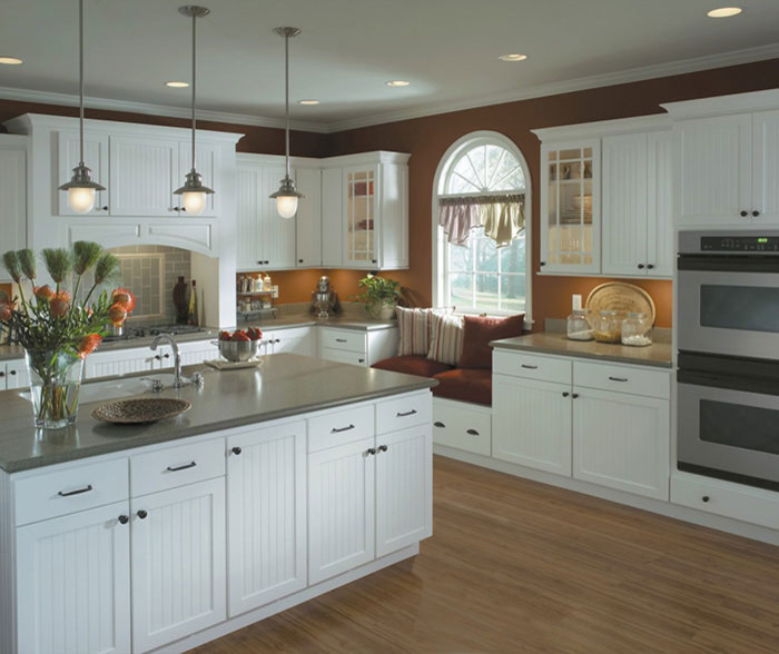 Modern inredning av ett stort kök, med en undermonterad diskho, skåp i shakerstil, vita skåp, bänkskiva i kalksten, blått stänkskydd, stänkskydd i porslinskakel, rostfria vitvaror, ljust trägolv, en köksö och brunt golv