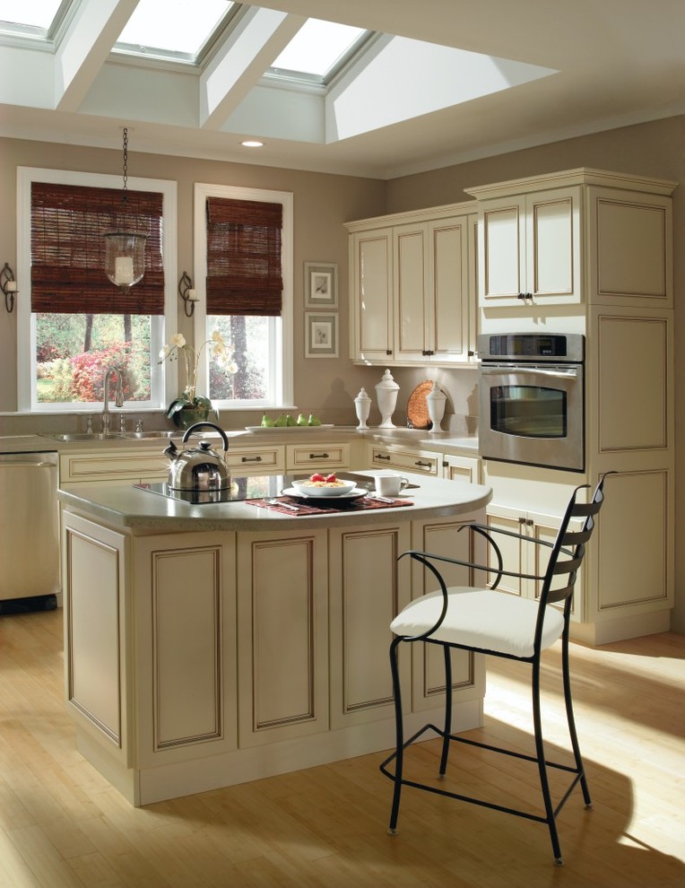 Mittelgroße Klassische Wohnküche in L-Form mit beigen Schränken, Küchengeräten aus Edelstahl und hellem Holzboden in Sonstige
