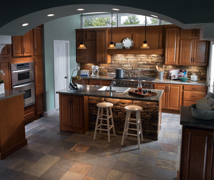 Mid-sized elegant u-shaped slate floor eat-in kitchen photo in Dallas with a drop-in sink, raised-panel cabinets, medium tone wood cabinets, granite countertops, brown backsplash, stone tile backsplash, stainless steel appliances and an island