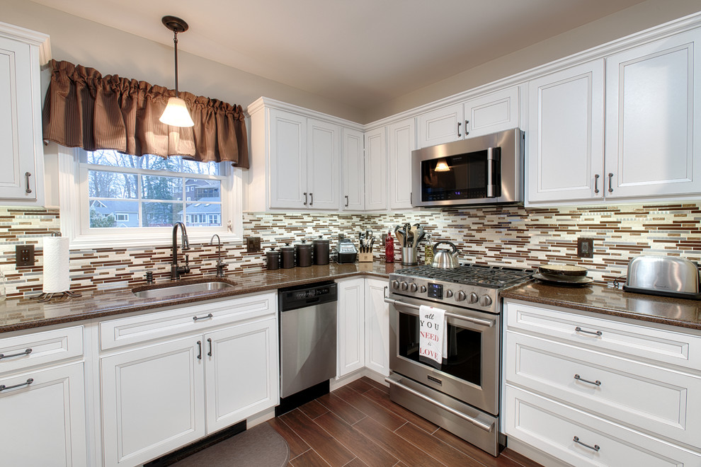 Inspiration for a large transitional u-shaped brown floor and porcelain tile open concept kitchen remodel in New York with an undermount sink, recessed-panel cabinets, white cabinets, quartz countertops, beige backsplash, stainless steel appliances, a peninsula and matchstick tile backsplash