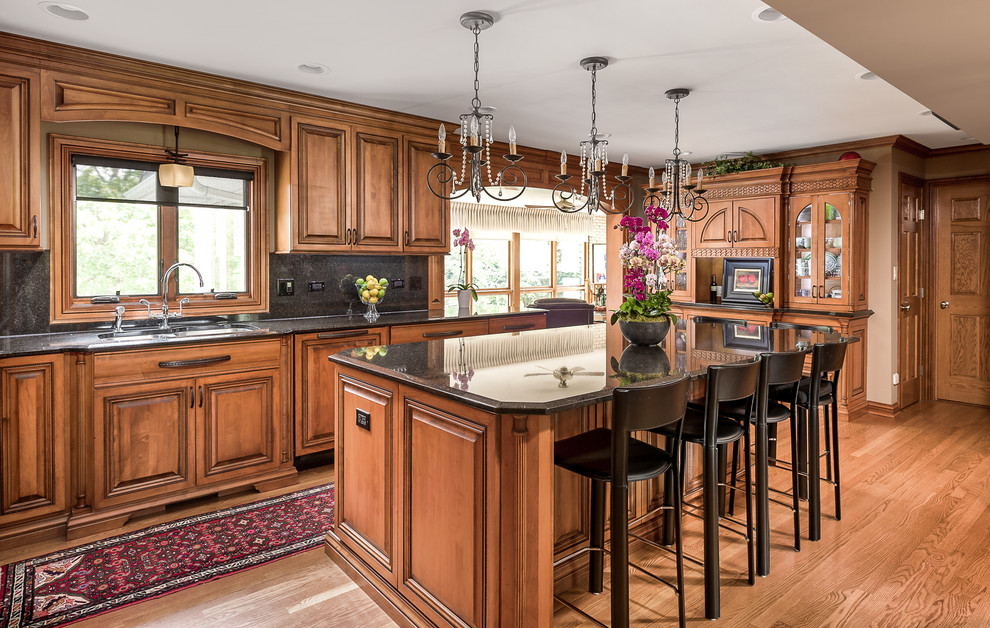 Design ideas for a traditional kitchen in Chicago with raised-panel cabinets, medium wood cabinets, black splashback, integrated appliances, medium hardwood flooring, an island and brown floors.