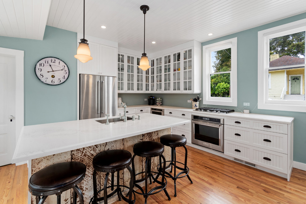 Beach style l-shaped kitchen in Other with a submerged sink, recessed-panel cabinets, white cabinets, medium hardwood flooring, an island, brown floors and white worktops.