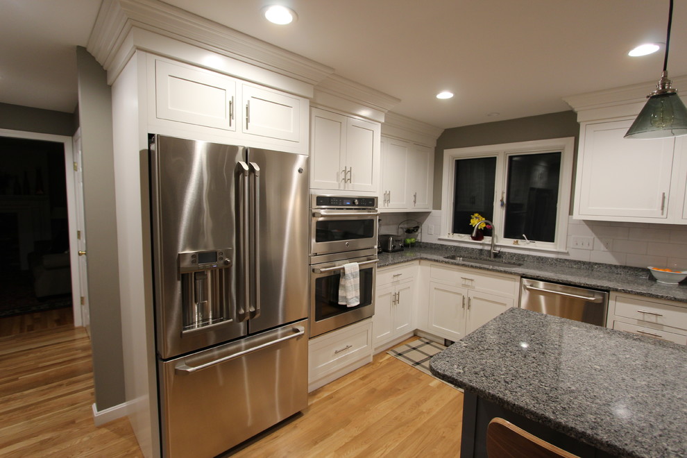 Exempel på ett mellanstort klassiskt kök, med en undermonterad diskho, skåp i shakerstil, vita skåp, granitbänkskiva, vitt stänkskydd, stänkskydd i tunnelbanekakel, rostfria vitvaror, mellanmörkt trägolv och en köksö