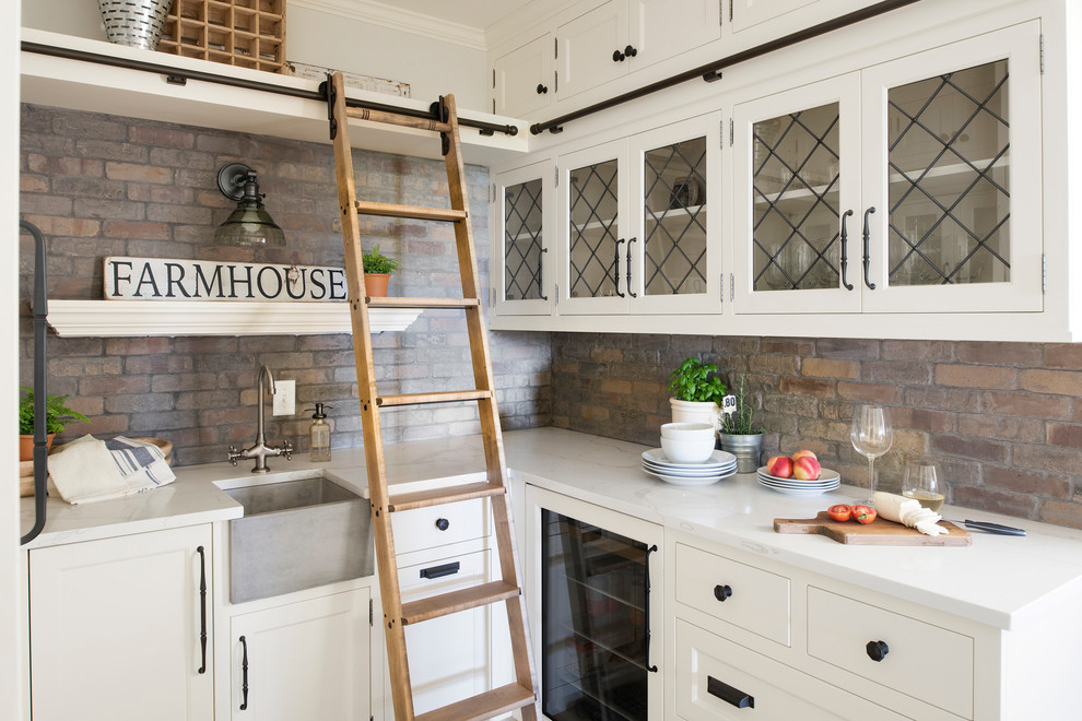 Large rural l-shaped kitchen pantry in Minneapolis with a belfast sink, white cabinets, multi-coloured splashback, brick splashback, stainless steel appliances, an island and white worktops.