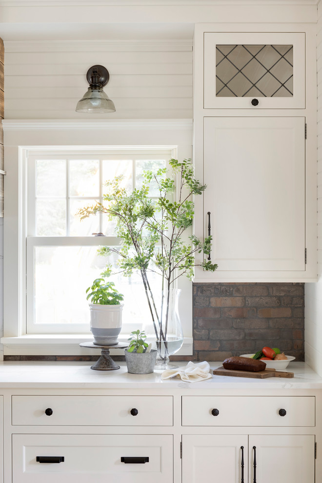 Lantlig inredning av ett stort vit vitt l-kök, med en rustik diskho, vita skåp, flerfärgad stänkskydd, stänkskydd i tegel, rostfria vitvaror och en köksö