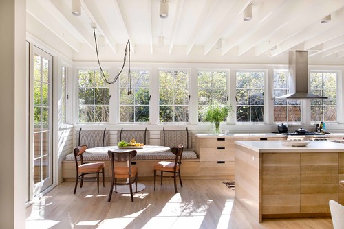 Kitchen with table and chairs, bathed in natural light, featuring white color scheme.
