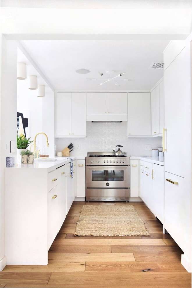 ニューヨークにあるコンテンポラリースタイルのおしゃれなコの字型キッチン (フラットパネル扉のキャビネット、白いキャビネット、白いキッチンパネル、パネルと同色の調理設備、無垢フローリング) の写真