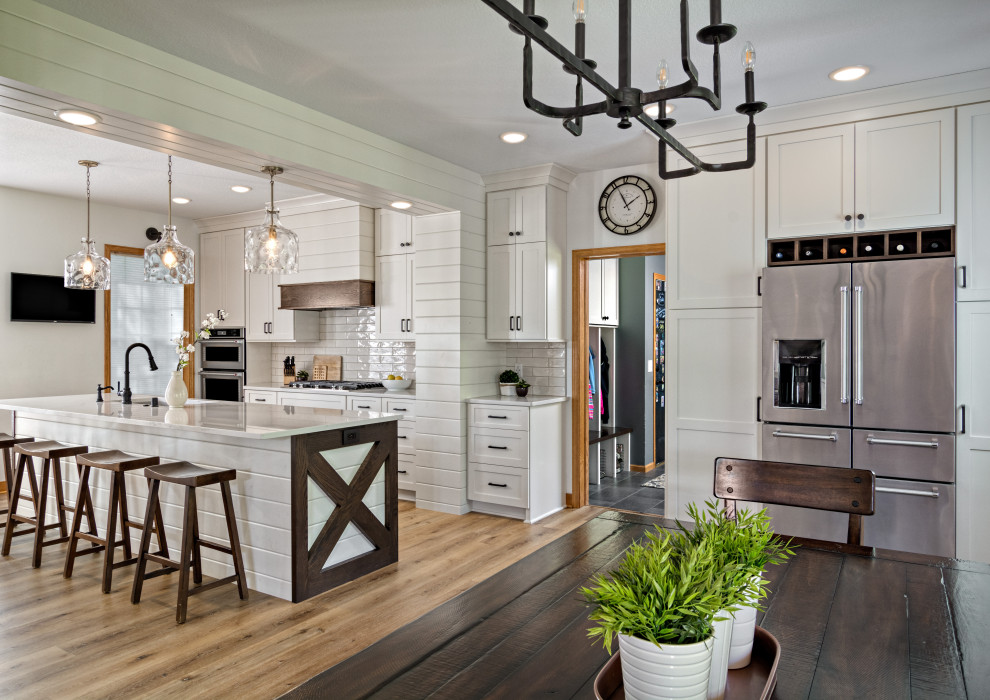 Inspiration for a large country single-wall light wood floor and brown floor open concept kitchen remodel in Minneapolis with an undermount sink, shaker cabinets, white cabinets, quartz countertops, white backsplash, ceramic backsplash, stainless steel appliances, an island and white countertops