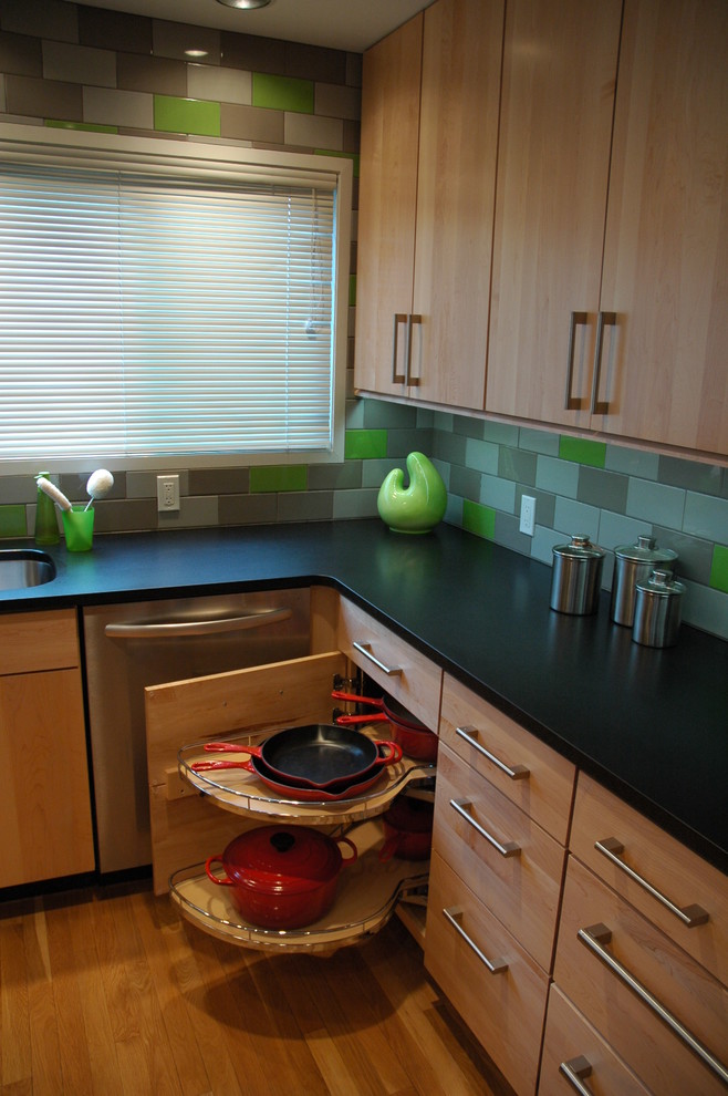Medium sized contemporary l-shaped kitchen/diner in Other with a submerged sink, flat-panel cabinets, light wood cabinets, granite worktops, green splashback, porcelain splashback, stainless steel appliances, light hardwood flooring and an island.