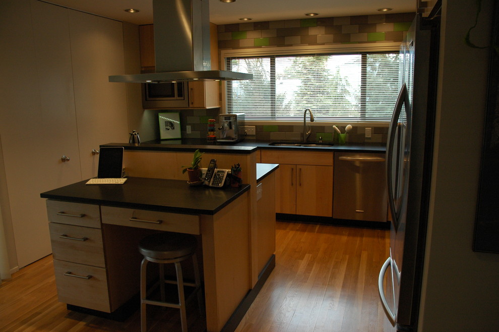 Idéer för ett mellanstort modernt kök, med en undermonterad diskho, släta luckor, skåp i ljust trä, granitbänkskiva, grönt stänkskydd, stänkskydd i porslinskakel, rostfria vitvaror, ljust trägolv och en köksö