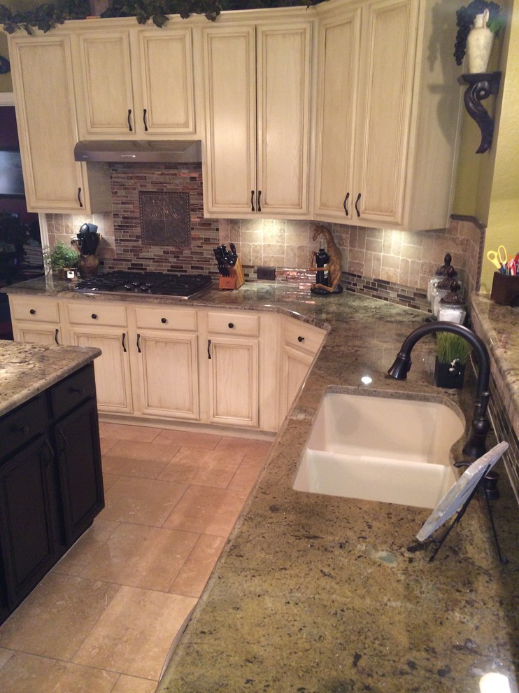 Elegant l-shaped eat-in kitchen photo in Dallas with an undermount sink, raised-panel cabinets, distressed cabinets, granite countertops, beige backsplash, stone tile backsplash and stainless steel appliances