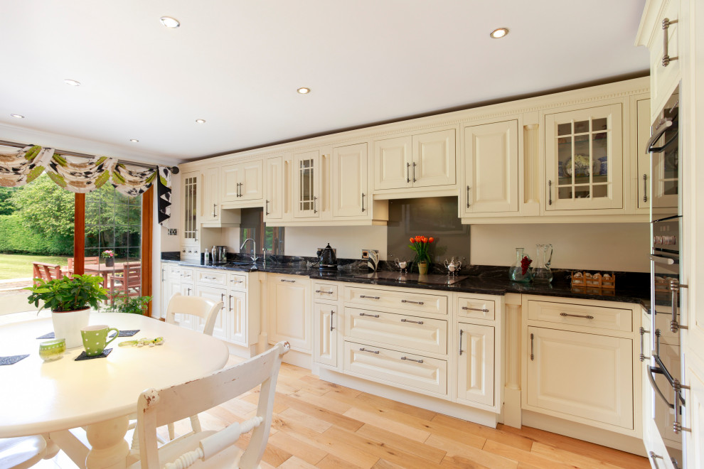 Rural kitchen/diner in Kent with a built-in sink, shaker cabinets, white cabinets, marble worktops, light hardwood flooring and black worktops.