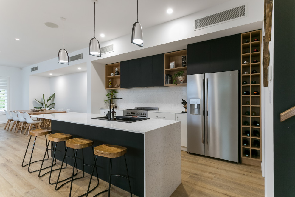 Inspiration for a large contemporary galley open plan kitchen in Adelaide with a built-in sink, white cabinets, engineered stone countertops, white splashback, stone slab splashback, stainless steel appliances, light hardwood flooring, an island, multi-coloured floors and white worktops.