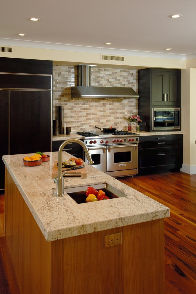 Bild på ett funkis kök, med rostfria vitvaror, granitbänkskiva, svarta skåp och stänkskydd i tunnelbanekakel