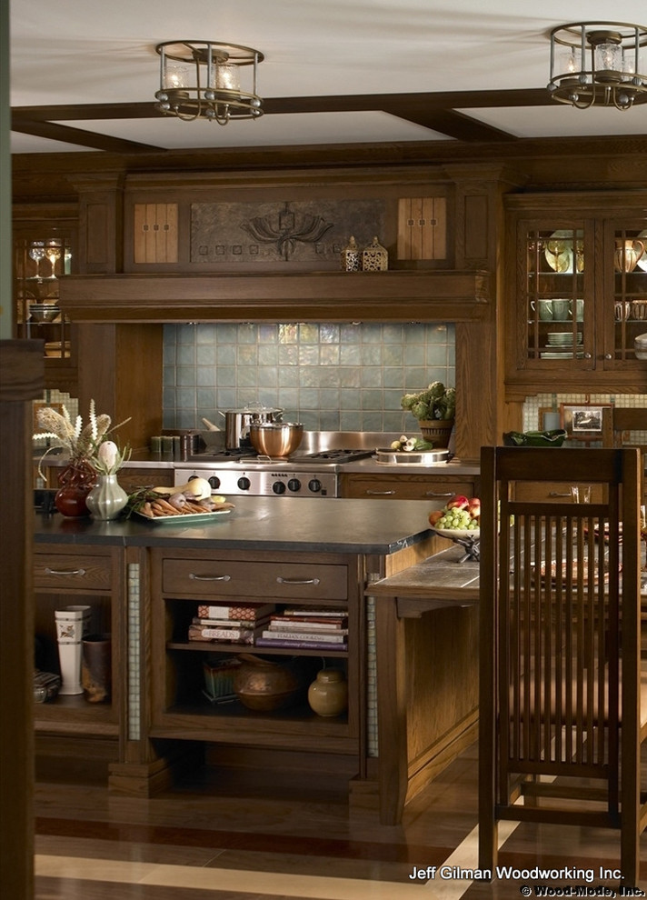 Cette image montre une cuisine américaine parallèle craftsman en bois foncé avec un évier encastré, un placard à porte plane, un plan de travail en stéatite, une crédence bleue et un électroménager en acier inoxydable.