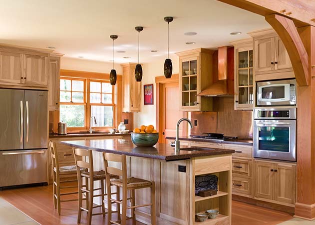 Klassisk inredning av ett stort brun brunt kök, med en nedsänkt diskho, luckor med glaspanel, skåp i ljust trä, bänkskiva i akrylsten, stänkskydd med metallisk yta, stänkskydd i metallkakel, rostfria vitvaror, mellanmörkt trägolv, en köksö och brunt golv