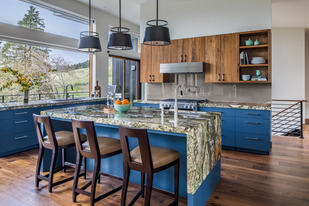 Foto på ett mellanstort rustikt flerfärgad kök, med en undermonterad diskho, släta luckor, blå skåp, granitbänkskiva, glaspanel som stänkskydd, rostfria vitvaror, en köksö, grått stänkskydd, mörkt trägolv och brunt golv