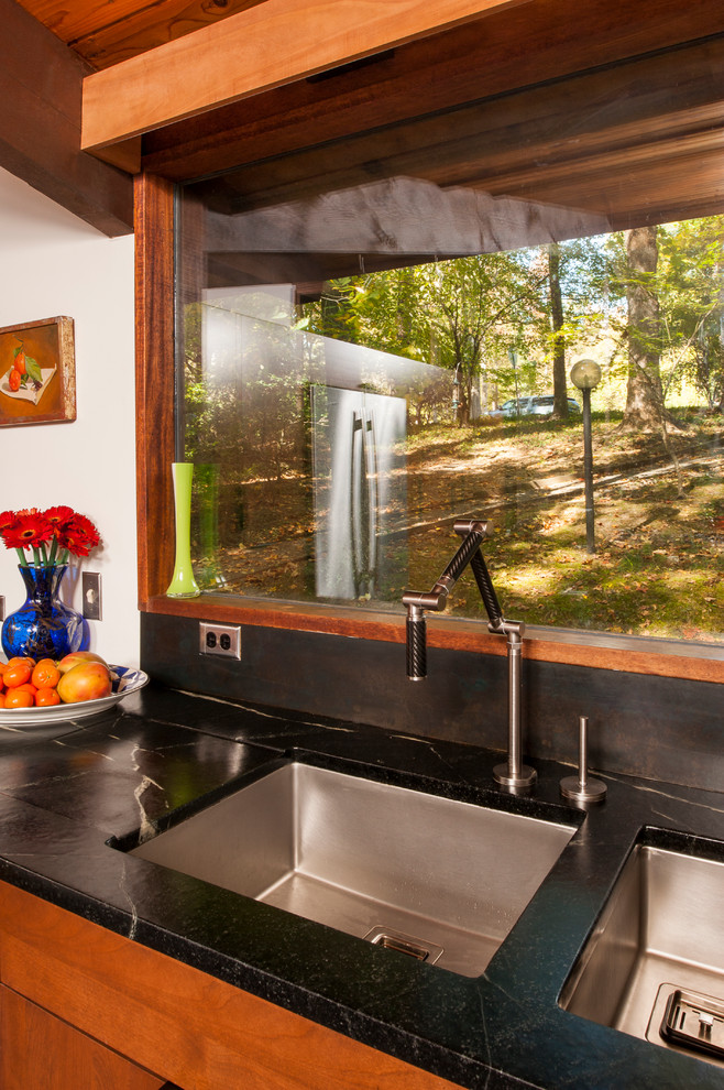 Cette image montre une cuisine américaine design en U et bois brun de taille moyenne avec un évier 2 bacs, un placard à porte plane, un plan de travail en stéatite, un électroménager en acier inoxydable, un sol en liège et une péninsule.