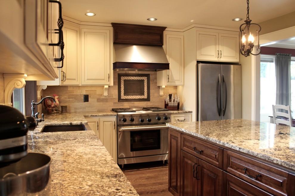 Example of a tuscan l-shaped eat-in kitchen design in Seattle with a farmhouse sink, raised-panel cabinets, dark wood cabinets, granite countertops, beige backsplash, metal backsplash and stainless steel appliances